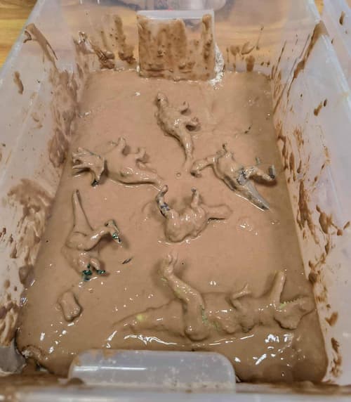 muddy dinosaur sensory play activity in a sensory bin