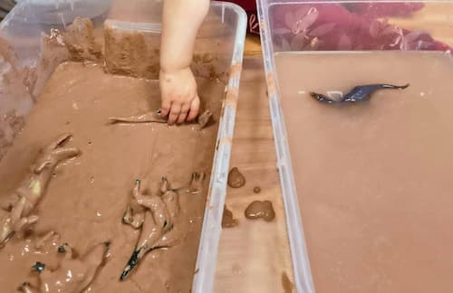 toddlers exploring a muddy sensory bin with dinosaurs
