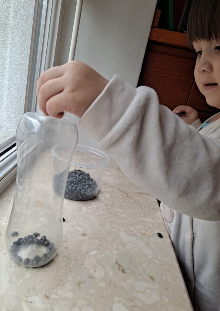 Toddler doing Montessori scooping activity with beans and bottle
