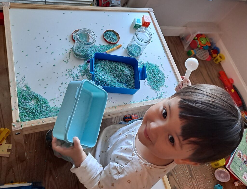 toddler scooping colored rice activity