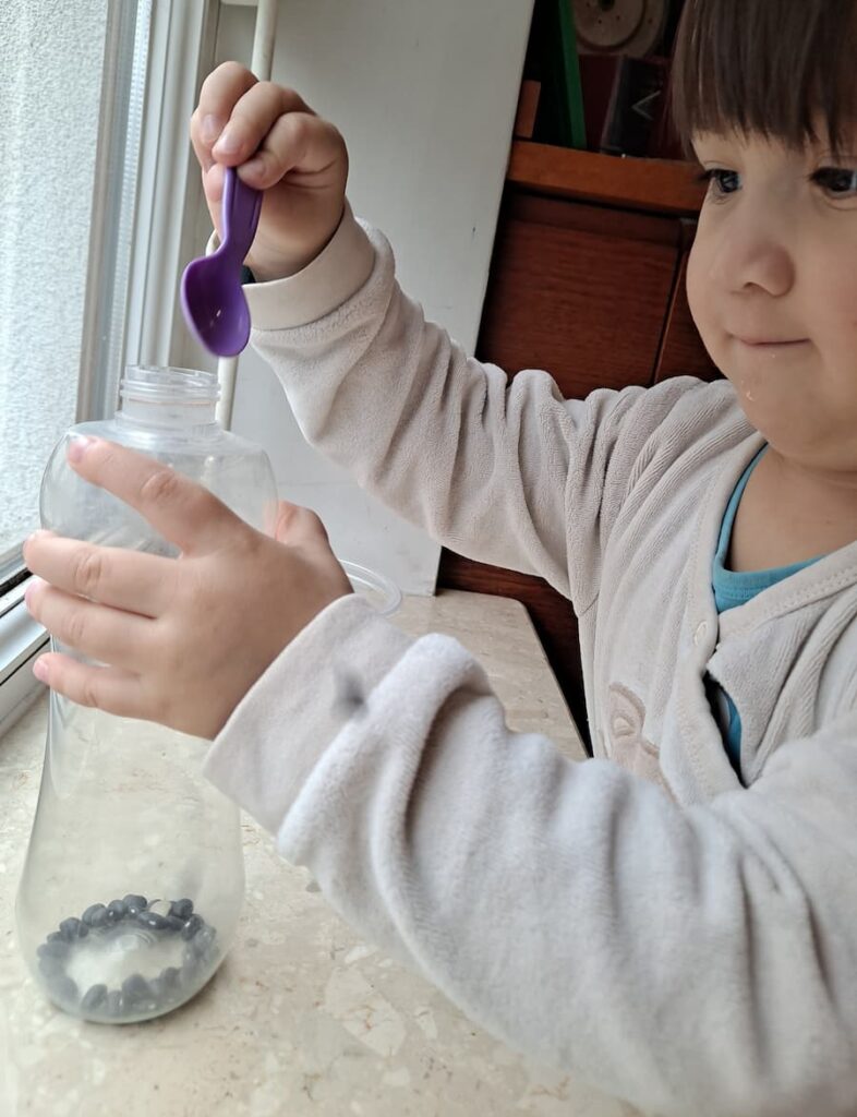 Toddler doing Montessori scooping activity with beans and bottle