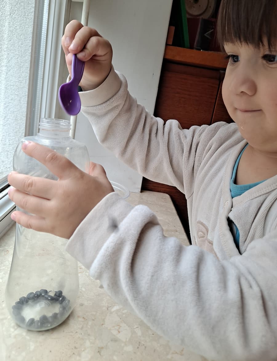 Toddler doing Montessori scooping activity with beans and bottle