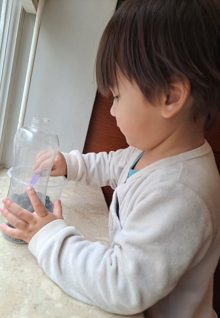 Toddler doing Montessori scooping activity with beans and bottle
